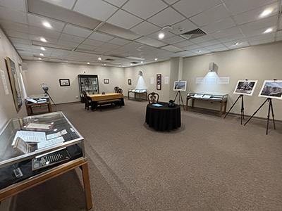 Photograph of a the exhibit room with exhibit cases in the middle of the room and along the walls, and enlarged photographs displayed on easels.