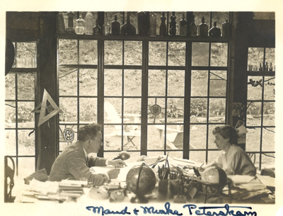 Maud & Miska Petersham in their Woodstock home studio sitting across a work table from one another in front of a large picture window. A handwritten caption below the image reads: Maud and Miska Petersham.
