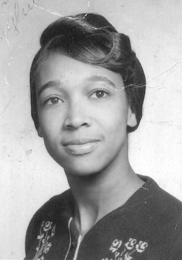 Grayscale portrait depicting an African-American woman from the shoulders up.  She is wearing a dark sweater with a lighter flower design across the front.  Her hair is swept up and pinned.  Her face is turned toward the camera with a relaxed expression.  She is looking beyond the camera.  There are some creases in the photo. 