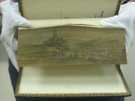 White-gloved hands fanning the fore-edge of a book showing the hidden painting. 