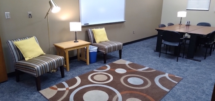 photo of two cloth chairs with table and lamp between with a rug. To the side is a long table with chairs.