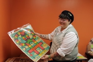 Photograph of Jaq Jefcoat standing in an office holding a poster from the collection.