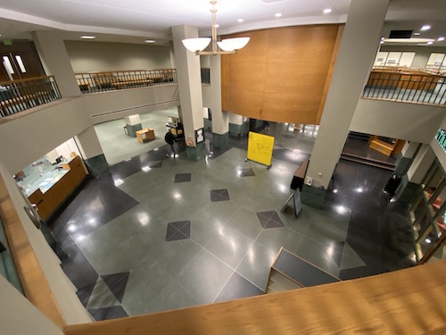 Overhead photo of the lobby of Cook Library, taken from the second floor. Floor on the lower level is green and black with large white columns around the room. At the top of the photo are railings from the balcony that overlooks the first floor. On the left side of the photo is the circulation desk and to the right is the entrance to Starbucks.